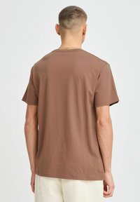 Bruine katoenen t-shirt met ronde hals en korte mouwen, zachte textuur en een relaxte pasvorm, gezien vanuit de achterkant.