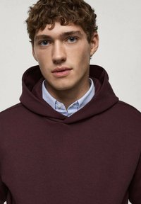 Bordowy hoodie z dużym kapturem, miękką fakturą i warstwą jasno-niebieskiej koszuli z kołnierzykiem pod spodem. Posiada luźny krój.