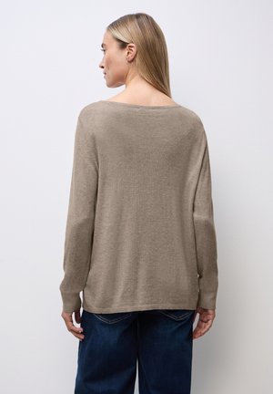 Beige pletený svetr s volným střihem, širokým výstřihem, dlouhými rukávy a žebrovanými manžetami. Nosený přes volné modré džíny, které ukazují jemnou texturu.
