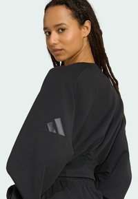 Sweatshirt noir oversize avec des manches longues et une taille côtelée. Présente un motif triangulaire texturé sur la manche et un col rond.