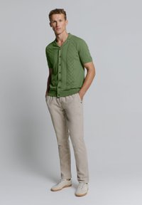 Groen gebreid shirt met korte mouwen en een gestructureerd ruitpatroon, met knoopsluiting, gecombineerd met lichtbeige broeken en witte sneakers.