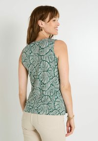 Top sin mangas verde con patrones de hojas blancas, hecho de material ligero. Presenta un escote curvado y una silueta ajustada.