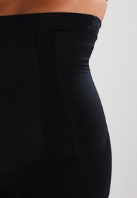 Mustat korkeavyötäröiset legginsit, jotka on valmistettu joustavasta kankaasta. Niissä on sileä pinta ja sivupaneeli yksityiskohtia.