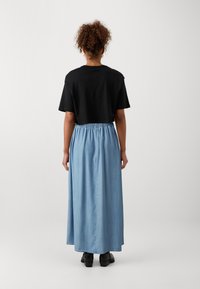 Camiseta negra corta de manga corta combinada con una falda larga de denim azul claro con cintura elástica. El calzado es negro.