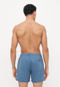 Blå badeshorts med elastisk midje, baklomme og glatt tekstur, med et enkelt design og ingen synlige mønstre.