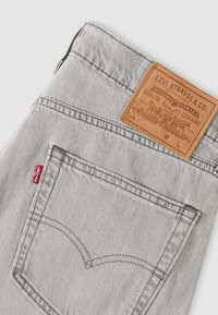 Πίσω τσέπη από ανοιχτό γκρι τζιν με κόκκινη ετικέτα Levi's και καφέ δερμάτινη ετικέτα με την επωνυμία Levi Strauss & Co. στη μέση.