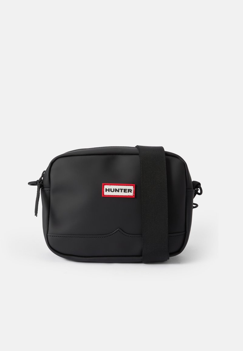 Čierna crossbody taška vyrobená z hladkého, matného materiálu s červenou a bielou nášivkou "HUNTER" a nastaviteľným čiernym remienkom.