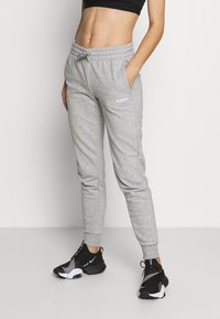 Grå mjukisbyxor med elastisk midja, sidofickor och vit logotypdetalj på vänster lår. Bärs med svarta träningsskor.