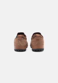 Sneakers in suede marrone con suole in gomma, caratterizzati da pannelli posteriori texture, linguette di supporto e rivestimento interno nero. Branding discreto sulla scarpa.