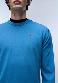 Lichtblauw langslıef shirt met een gestructureerde afwerking. Heeft een kleine geborduurde Noorse vlag op de linkerkant van de borst. Ronde halslijn.