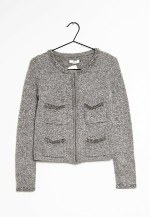 Grijze gebreide langarmige cardigan met ritssluiting aan de voorkant, vier voorzakken en decoratieve kralen op de kraag, zomen van de zakken en manchetten, hangend aan een zwarte hanger.