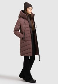 Polstret frakke i støvet mauve med chevron-syninger, frontlynlås, justerbar hætte og lynlåslommer i siden, parret med sorte flagrende bukser og støvler.