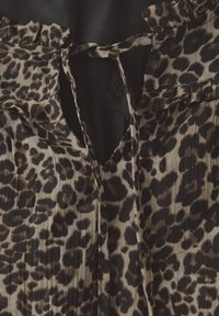 Blusa con stampa leopardata caratterizzata da bordi arricciati, accenti in tessuto nero e un dettaglio a oblò sullo scollo. Le pieghe testurizzate esaltano il design.