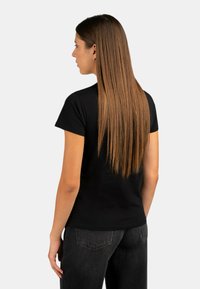 T-shirt nera a maniche corte con un design aderente, realizzata in un tessuto liscio, abbinata a jeans grigio scuro. Il tessuto è semplice, senza motivi.