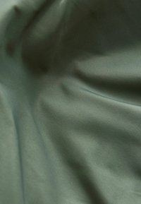 Textil mit Struktur in Olivgrün mit einer glatten, matten Oberfläche. Zeigt sanfte Falten und leichte Farbvariationen auf der Fläche.