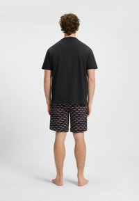 T-shirt noir à manches courtes associé à un short noir avec un motif de logo répétitif rouge et blanc. Porté par une personne vue de dos.