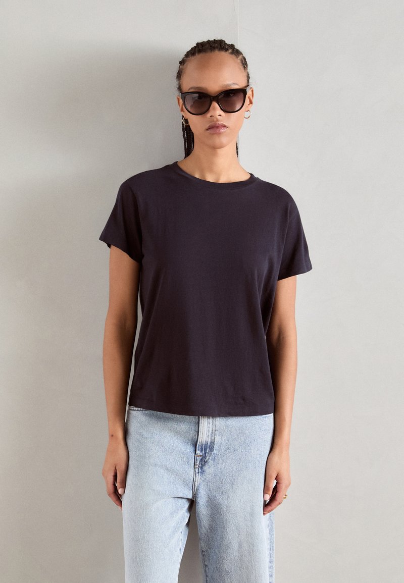 Zwarte T-shirt met korte mouwen van zachte stof, met een ronde halslijn en een losse pasvorm, gecombineerd met lichtblauwe hoge taille jeans.