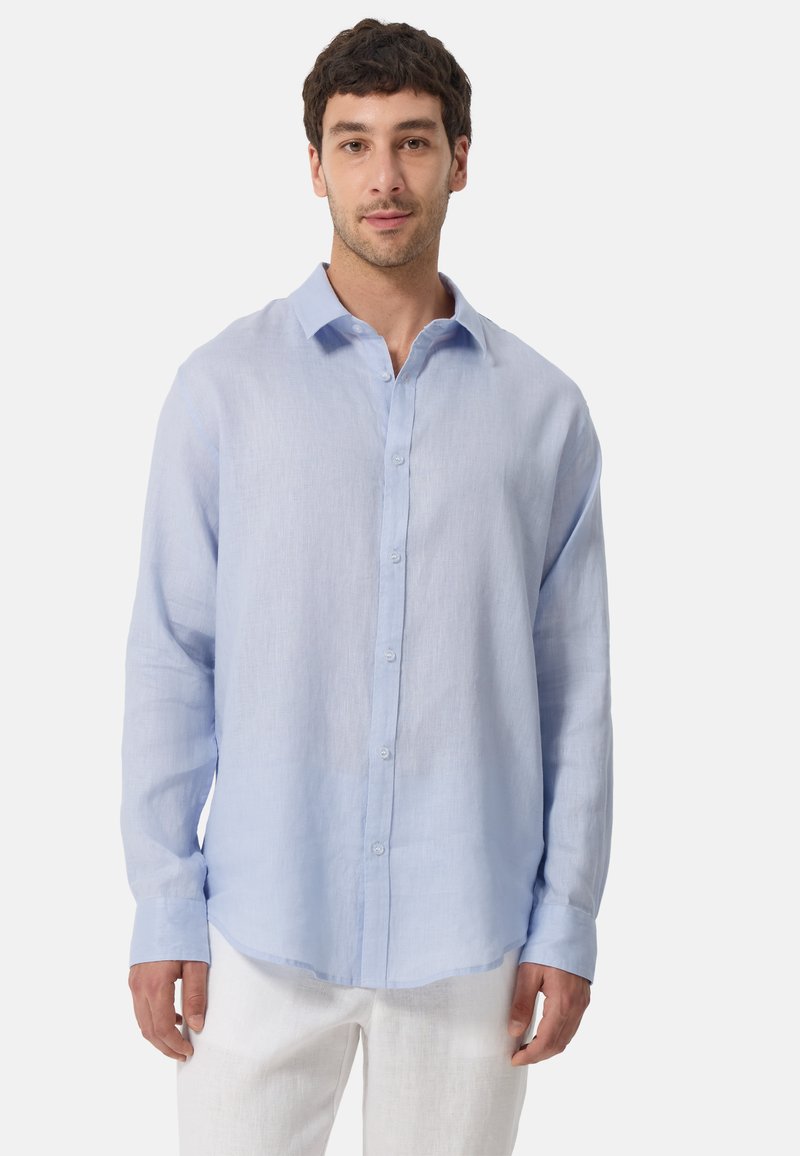 Chemise en lin bleu clair à manches longues avec un design à boutons sur le devant, un col pointu et un ourlet arrondi, associée à un pantalon blanc.