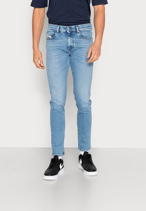 Jeans de mezclilla azul claro con un corte slim, que presentan un diseño clásico de cinco bolsillos y una textura ligeramente desgastada, combinados con zapatillas negras.