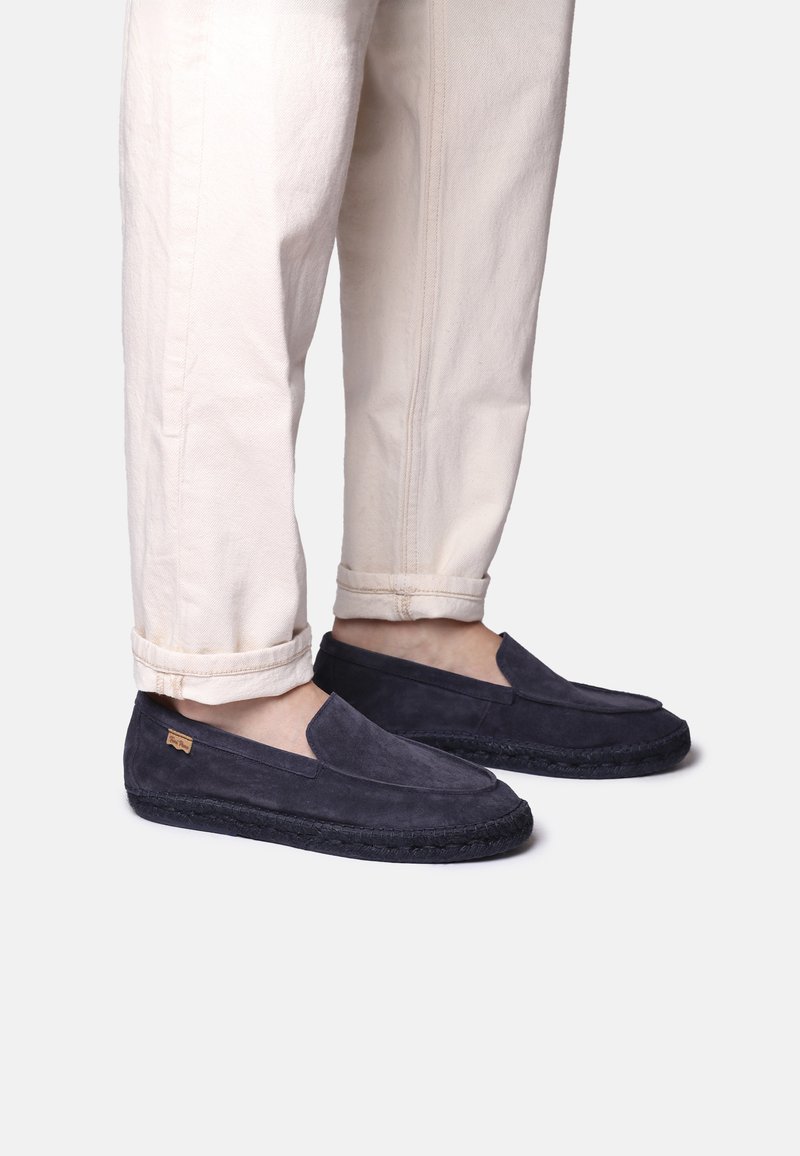 Námořnické semišové boty na slip-on s texturovaným svrškem a pletenou tkaninovou podešví, spárované s vyhrnutými krémovými kalhotami.