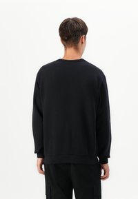 Black sweatshirt with long sleeves, ribbed neckline and cuffs, soft texture, and a relaxed fit. Worn backwards, revealing solid color.