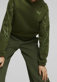 Groene hoodie en bijpassende broek gemaakt van zachte stof. Heeft een subtiel PUMA-logo en lichtgroene contourontwerpen op de mouwen. Elastische manchetten.