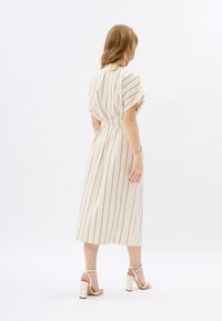 Cremestreifenkleid mit einem taillierten Gürtel, kurzen Ärmeln und Midi-Länge. Tragen mit hellfarbigen, absatzsandalen. Glatte Textur.
