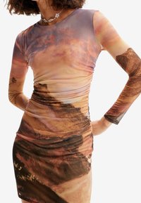 Robe mini froncée en tissu transparent avec un imprimé paysage abstrait multicolore, manches longues et silhouette ajustée.