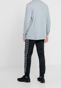 Grå långärmad skjorta med rundad hals, kombinerad med svarta träningsbyxor med vita sidostråk och ett logomönster, samt svarta sneakers.