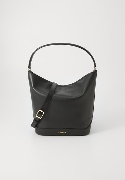 Sac à main en cuir noir avec un design courbé. Doté d'une longue bandoulière et d'une boucle en or. Logo "SANDRO" embossé sur la base. Texture lisse.