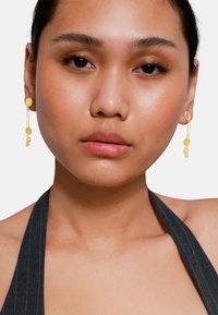 Boucles d'oreilles pendantes en or avec des formes circulaires et ovales, dotées d'un design en maillons. Les boucles d'oreilles pendent délicatement, capturant la lumière pour un éclat subtil.