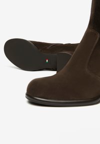 Stivali ankle in suede marrone con punta tonda, zip laterale e suola in gomma. Presentano un tacco nero a contrasto e un discreto logo sulla suola.
