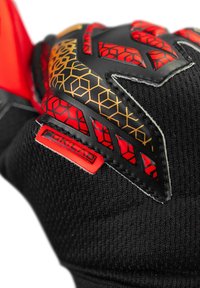 Guanto nero caratterizzato da una superficie testurizzata con accenti geometrici rossi e arancioni, grip in gomma sul palmo e un'etichetta logo a contrasto.