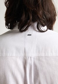 Witte shirt, lichtgewicht stof met een gladde textuur, met een klassieke kraag en een klein zwart label aan de achterkant van de nek.