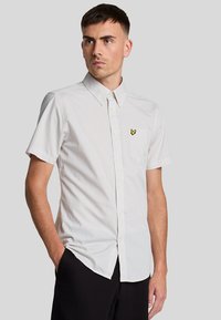 Camicia a maniche corte a quadri di colore grigio chiaro con un logo a farfalla gialla sul lato sinistro del petto e colletto button-down.