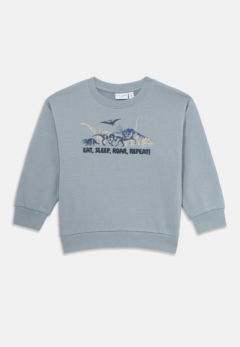 Lyseblå langermet sweatshirt med illustrasjoner av forskjellige dinosaurer og teksten "ETT, SOV, RÅL, GJENTAR!" over brystet.