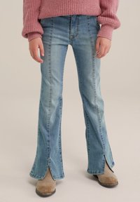 Ljusblå, högmidjade jeans med utsvängda ben och sidoöppningar. Tillverkade av denim med synliga sömnadsdetaljer, i kombination med tanfärgade ankelskor.