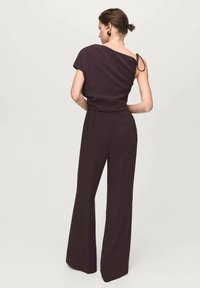 Donkerpaars jumpsuit met wijde pijpen en een asymmetrische halslijn. Gemaakt van zachte stof met een getailleerde taille en een enkele verstelbare band.