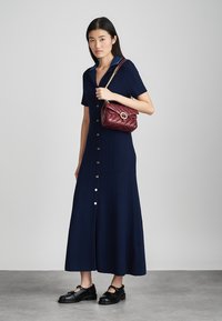 Abito a coste blu navy con maniche corte e chiusura a bottoni. Abbinato a una borsa trapuntata bordeaux e mocassini neri spessi. Tessuto liscio.