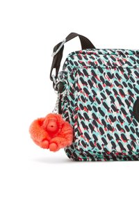 Rechteckige Tasche mit einem bunten Muster aus schwarzen, roten und türkisfarbenen Formen; ausgestattet mit einem braunen Tragegurt und einem orangefarbenen, fuzzy Affenanhänger.