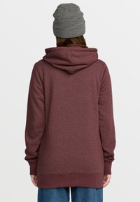 Sweat à capuche bordeaux avec une coupe décontractée, doté d'une grande capuche, de manches longues et d'un ourlet côtelé. Associé à un bonnet en tricot noir et blanc.