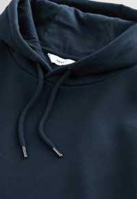 Sudadera con capucha en un azul marino oscuro, de corte relajado, material de algodón, bolsillo canguro frontal, capucha con cordón y terminales metálicos en los cordones.