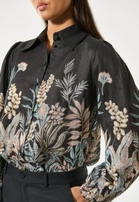 Black blouse with floral embroidery in pastel colors, featuring a classic collar, button-up front, and slightly puffed sleeves.