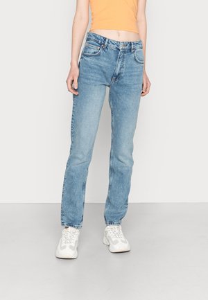 Jeans de denim azul claro com um corte direito, design de cinco bolsos e um sutil desgaste, combinados com ténis brancos e uma t-shirt cropped laranja.