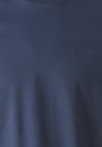 Námořnická modrá bavlněná tričko s kulatým výstřihem a decentním embosovaným logem "JOOP!" na přední straně. Hladká textura s přiléhavým siluetou.