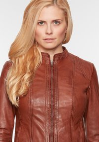 Braune Lederjacke mit hohem Kragen, mit genähten Details an der Front und einem zentralen Reißverschluss. Glatte Textur und taillierte Passform.