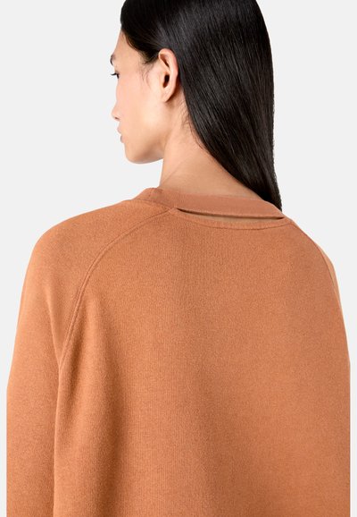 Rust-colored sweater featuring a textured knit, rounded neckline, and a back cutout detail. Designed with raglan sleeves for easy movement.
