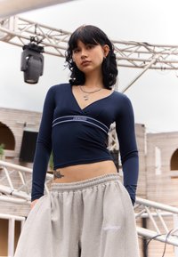 Marineblaues Langarmoberteil mit V-Ausschnitt und weißen Bänder-Details, kombiniert mit lockeren grauen Jogginghosen mit gesticktem Logo.