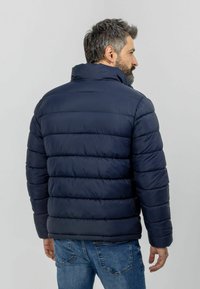 Veste rembourrée marine avec un col haut, un design matelassé et des coutures contrastantes. Présente une texture lisse et une coupe décontractée.