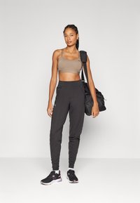 Soutien-gorge de sport marron, joggeurs noirs fuselés et chaussures de sport noires. Les caractéristiques incluent une texture lisse, un design ajusté et un sac noir portable.